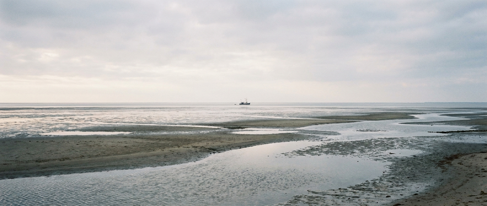 Urlaub zu zweit auf der Nordseeinsel Pellworm – weiter Blick über das Wattenmeer mit Krabbenkutter am Horizont